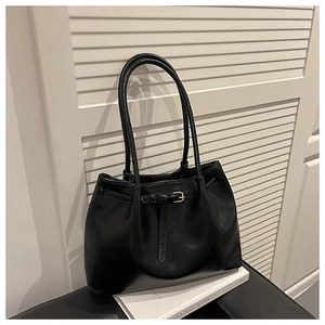 Close-up of black glossy leather tote bag with long handles and elegant belt detail