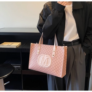 Close-up of pink tote bag featuring all-over M pattern and 3D metallic logo detail