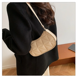 Close-up of beige quilted baguette bag with geometric stitching worn on shoulder