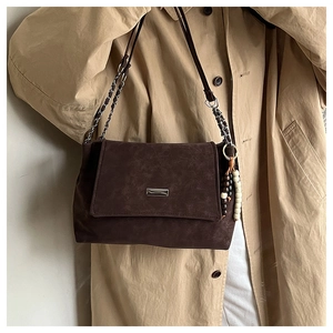 Detail of dark brown suede tote with chain strap and beaded charm on khaki trench coat