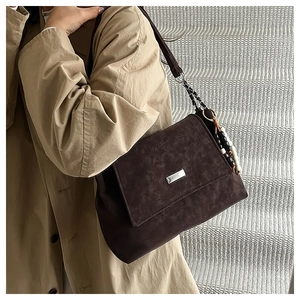 Detail of dark coffee suede tote bag featuring silver plate and beaded charm on khaki coat
