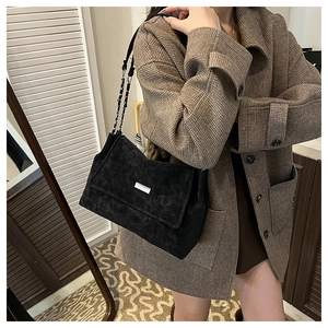 Détail d'un sac bandoulière vintage en daim noir avec plaque argentée et bandoulière chaîne