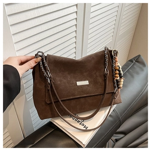 Détail d'un sac cabas en daim marron avec bandoulière en chaîne et pendentif en perles de bois