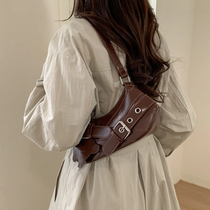 Deep brown glossy baguette bag with bear pendant shown on model in warm studio lighting