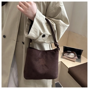 Close-up of brown suede bucket bag with knotted handle detail and embossed text