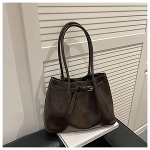 Detailed close-up of dark brown leather tote bag with gold buckle on white books