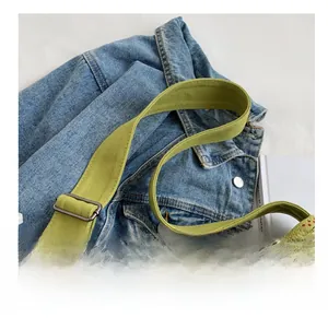 Detail of adjustable green canvas strap with retro typography and metal buckle on denim