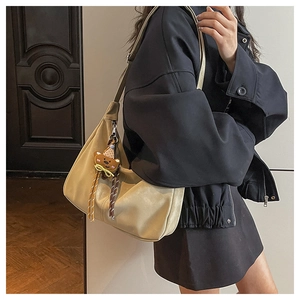 Close-up of a beige hobo bag with a cute brown bear charm and striped ribbon detail