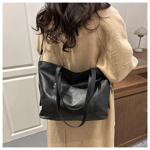 Rear view of model wearing a large black pebbled leather tote bag with an overcoat