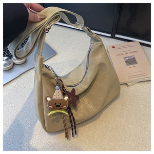 Detail of a beige crescent hobo bag with white stitching and cute teddy bear charm accessory