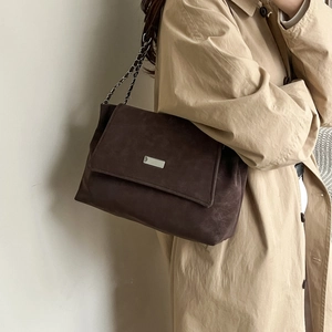 Grand sac cabas marron foncé en daim avec chaîne argentée et boucle sur un trench-coat
