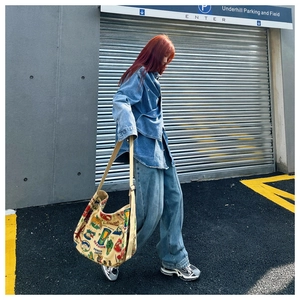 Street style view of a large vintage canvas tote bag with graffiti art on a denim outfit