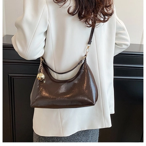 Detail of dark brown patent leather crescent bag with gold sphere charm and fashion logo