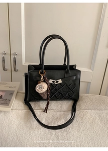 Détail du sac à main carré noir brodé avec motif matelassé et couronne sur canapé
