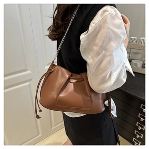 Detail of brown pleated shoulder bag with chain strap and drawstring tassel on a model