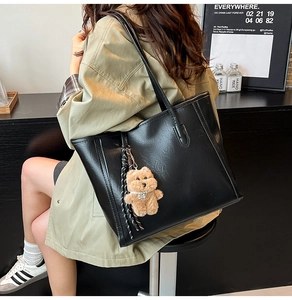 Detail of black faux leather tote bag with brown bear charm and woven tassel accent