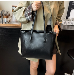 Detail of a black faux leather tote bag showing smooth oil-wax finish and long shoulder straps