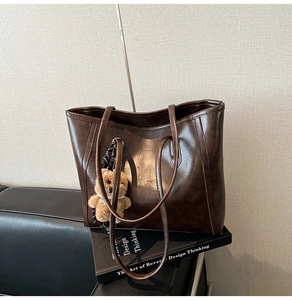 Detail of vintage brown oil wax leather tote bag featuring a cute teddy bear charm