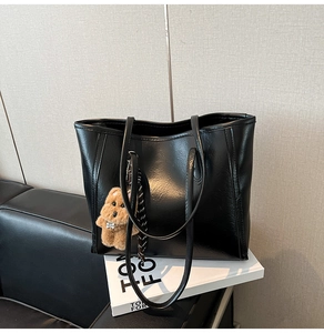 Detail of glossy black oil wax leather tote bag with a cute brown plush bear charm