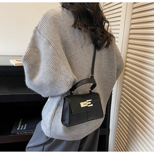 Detail of black leather square bag with gold buckle worn with a gray knit sweater