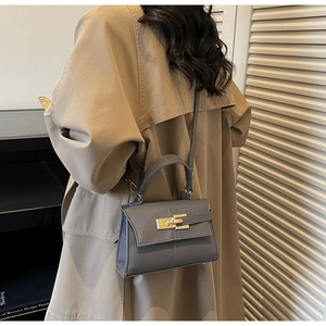 Sac à main trapèze en cuir gris avec fermoir doré présenté dans un cadre décontracté