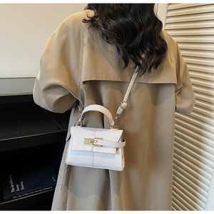 Détail du sac à main en cuir blanc crème avec fermoir doré porté avec un trench-coat