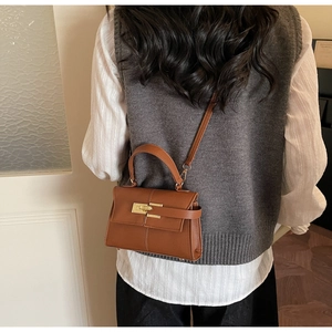 Détail du sac en cuir marron avec boucle dorée et bandoulière porté par un mannequin