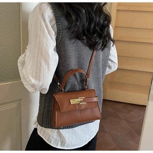 Gros plan du sac à main en cuir marron grainé avec fermoir doré porté par le mannequin