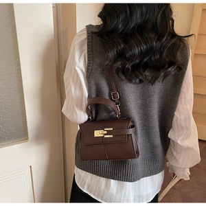 Détail du sac à main en cuir marron foncé avec fermoir doré sur une tenue grise