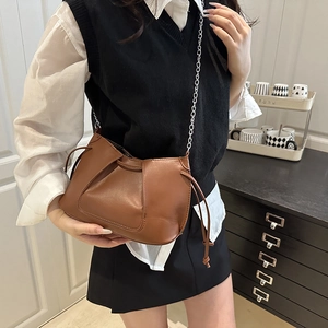 Bolso bandolera marrón con diseño fruncido y cadena plateada en un ambiente interior