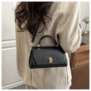 Detail of black textured leather handbag with gold metal lock worn on cream blazer