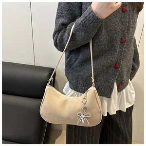 Detail of a beige hobo bag with rhinestone bow charm and slim shoulder strap