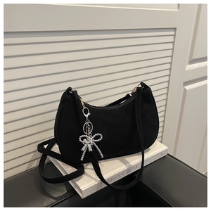 Detail of black suede crescent bag with silver beaded bow charm on a decorative book