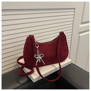 Detail of burgundy suede shoulder bag with silver bow heart pendant on a book