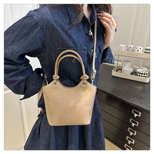 Close-up of khaki embossed bucket bag with cartoon patterns worn by a model in a cozy room