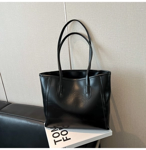 Macro shot of black tote bag featuring crinkled glossy leather texture and thin straps
