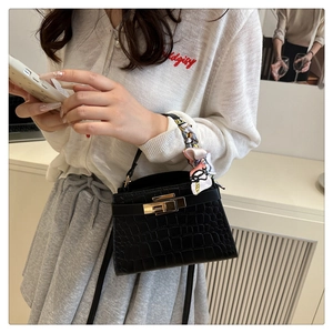 Detail of black crocodile texture handbag with gold clasp and silk scarf on handle