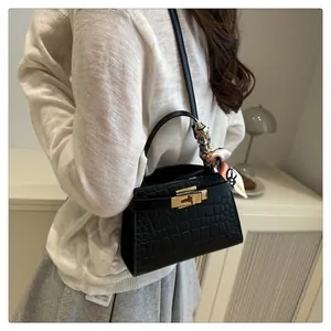 Detail of black crocodile texture handbag with gold metal clasp and floral silk scarf handle