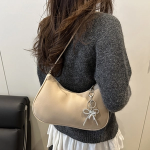 Fashionable beige crescent hobo bag with a silver bow charm shown on a shoulder