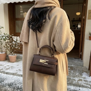 Sac Kelly en cuir grainé marron foncé avec boucle dorée dans une scène de rue d'hiver