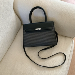 Detail of black patchwork handbag with metal twist lock and woven texture on a soft surface