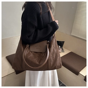 Close-up of large brown travel bag with wrinkled patent leather texture and logo detail