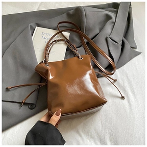 Détail d'un sac seau marron brillant avec poignée en chaîne métallique et cordon