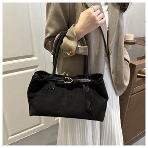 Detail of minimalist black suede tote bag with metal buckle and hanging tag accessory
