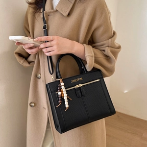 Sac bandoulière noir chic avec logo doré et breloque en bois sur modèle en manteau de laine