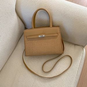 Straw and leather patchwork handbag with silver metal turn-lock on a beige sofa