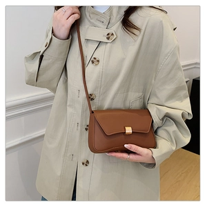 Detailed view of caramel leather crossbody bag with elegant gold buckle on beige trench coat