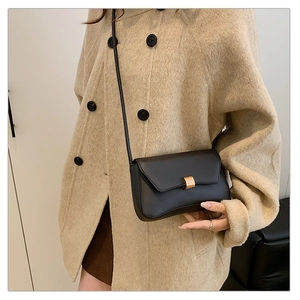 Close-up of minimalist black crossbody bag with gold buckle on a beige wool coat