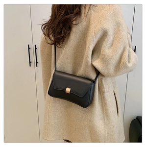 Close-up of minimalist black crossbody bag with gold metal buckle on beige coat