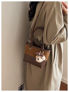 Detail of a brown leather and suede bucket bag featuring a cute teddy bear charm